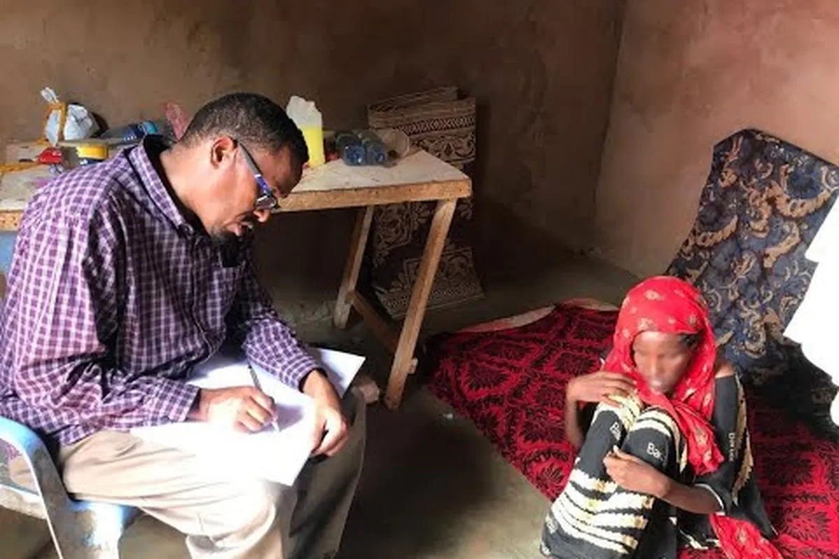 Dr. Takar writes notes while assessing a young woman during a home visit